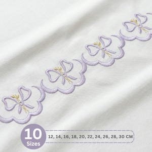 Può includere: Tessuto bianco con un delicato bordo ricamato con fiocchi lavanda ripetuti con accenti dorati. L'immagine include testo che indica 10 taglie disponibili, che vanno da 12 a 30 cm.