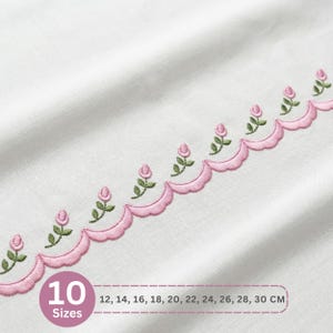 May include: White fabric with a scalloped pink embroidered border featuring pink rosebuds and green leaves. The image includes the text "10 Sizes" and measurements in centimeters: 12, 14, 16, 18, 20, 22, 24, 26, 28, 30 CM.