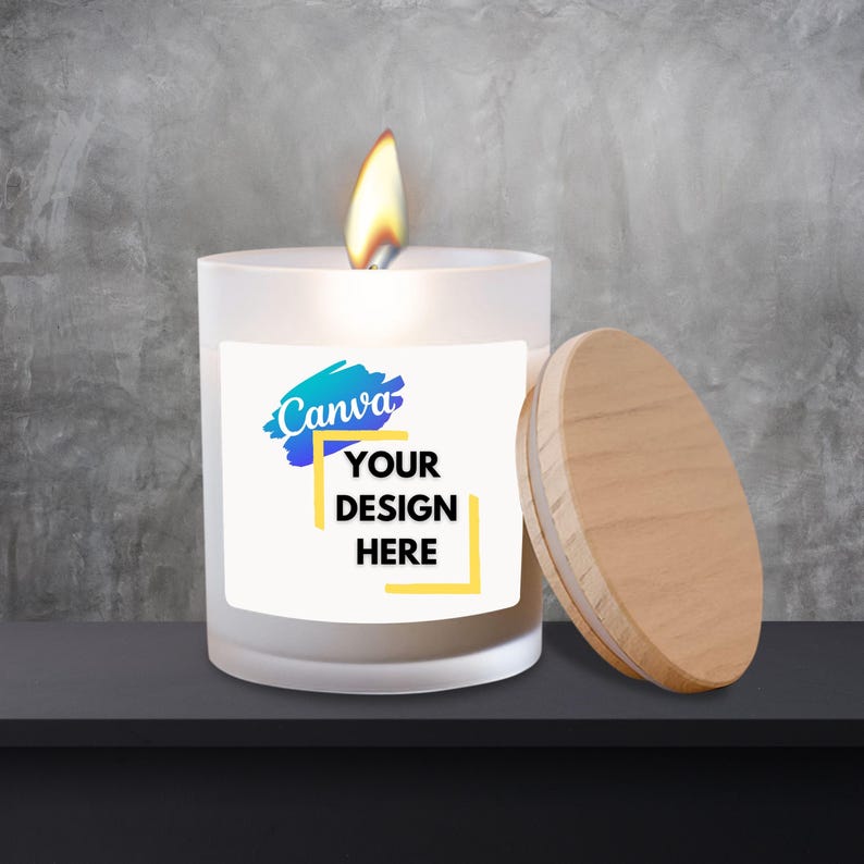Puede incluir: Una vela blanca encendida con tapa de madera. La vela tiene una etiqueta con el texto "Canva" y "YOUR DESIGN HERE". La vela est&aacute; sobre una superficie negra contra un fondo gris.