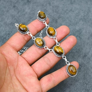 May include: A silver-toned necklace featuring oval-shaped tiger's eye gemstones. The gemstones are set in a decorative bezel and connected by a delicate chain. The necklace has a symmetrical design with a central pendant and smaller stones.