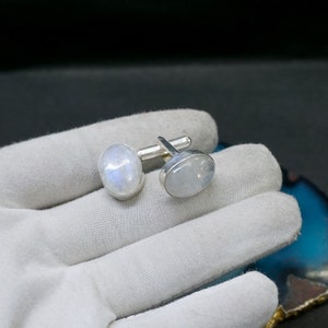 May include: A pair of silver cufflinks with oval-shaped moonstone inlays. The cufflinks are set in a silver frame and have a polished finish.