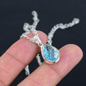 Puede incluir: Un collar de cadena de plata con un colgante en forma de lágrima con una piedra preciosa azul iridiscente.