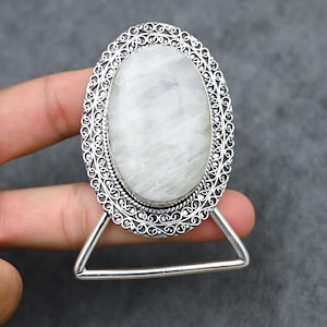 Op de afbeelding: Zilverkleurige ring met een grote, ovale, witte edelsteen. De edelsteen is gezet in een decoratieve filigraan-stijl frame. De ring heeft een uniek, open ontwerp.