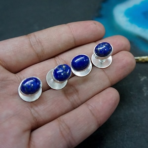 Peut inclure: Quatre boutons de manchette en argent avec des pierres ovales en lapis-lazuli. Les pierres sont d'un bleu profond avec des reflets dorés.
