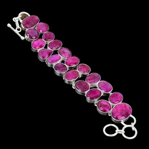 Op de afbeelding: Een zilveren armband met twee rijen ovale, levendige roze edelstenen. De edelstenen zijn gezet in individuele zilveren bezels en verbonden door zilveren schakels. De armband heeft een tuimelsluiting, tegen een zwarte achtergrond.