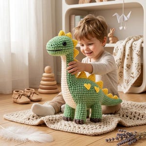 May include: A green and cream-colored crocheted dinosaur toy featuring a long neck, a textured body, and yellow heart-shaped patches along its back. The dinosaur has dark brown feet and a row of yellow triangular spikes running from its head to its tail.