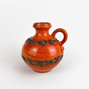 Peut inclure: Vase en céramique orange avec un motif noir. Le vase a un corps rond et une petite poignée.