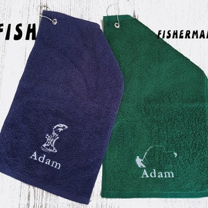 May include: Two personalised golf towels, one navy blue with a fish jumping out of the water and the name "Adam" embroidered on it, and one green with a fisherman casting a line and the name "Adam" embroidered on it.