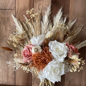 May include: A dried flower bouquet with white, pink, and brown flowers, and dried grasses. The bouquet is tied together with twine.