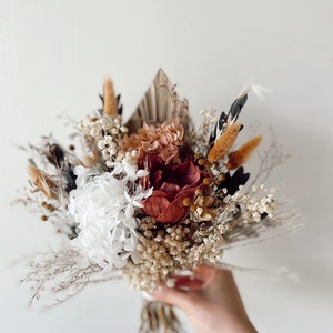 May include: A dried flower bouquet with white, pink, and burgundy flowers, dried grasses, and pampas grass.
