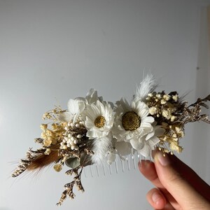 May include: A white hair comb decorated with dried white flowers, brown feathers, and small white berries.