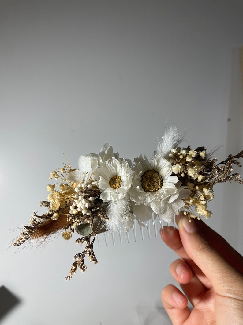 May include: A white hair comb decorated with dried white flowers, brown feathers, and small white berries.
