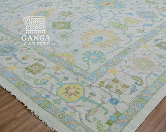 May include: A large, rectangular rug with a light grey background and a detailed floral pattern in shades of blue, yellow, and green. The rug has a light blue border and the text "GANGA CARPETS" in the corner.
