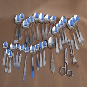 Puede incluir: Una colección de cucharas de plata, algunas con mangos adornados, dispuestas sobre una superficie marrón.