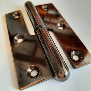 Puede incluir: Una bisagra de metal negro con un barril redondeado y un acabado pulido. La bisagra tiene dos placas con múltiples agujeros para tornillos.