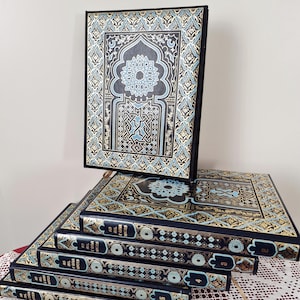 Può includere: Un set di sei libri con copertina rigida nera caratterizzati da intricati motivi geometrici dorati e azzurri. La copertina presenta un design ad arco con un motivo a stella centrale. I dorsi riportano numeri e il testo As Mil e Uma Noites.