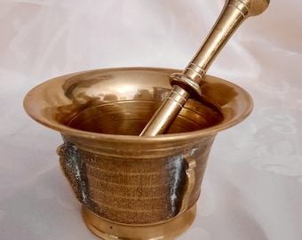 May include: A brass mortar and pestle set. The mortar is a bowl with a textured surface and the pestle is a smooth, rounded rod.