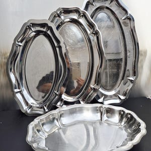 Op de afbeelding: Een set van vier zilverkleurige ovale serveerschalen. De schalen hebben een geschulpte rand. De grootste schaal is ongeveer 51 cm lang, de kleinste ongeveer 25 cm. Gemaakt van glanzend, reflecterend metaal.