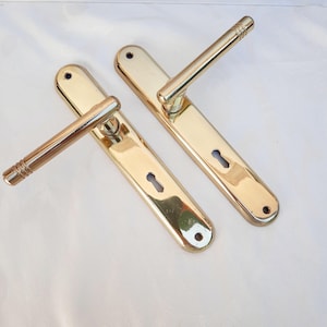 Peut inclure: Deux poignées de porte en laiton poli. Chaque poignée a une plaque arrière rectangulaire avec un trou de serrure et une poignée cylindrique. Les poignées sont orientées vers l'extérieur.