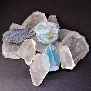 May include: A collection of sea glass in various shades of blue and white. The sea glass is arranged on a black surface.