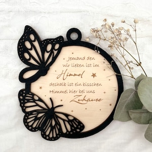 Könnte beinhalten: Ein runder Holzanhänger mit einem schwarzen Schmetterlingsdesign und dem Text "* Jemand den wir lieben ist im Himmel deshalb ist ein bisschen Himmel hier bei uns Zuhause *"