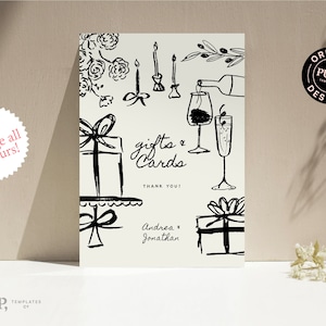 May include: A black and white illustrated wedding sign with the text "gifts & cards" and "thank you". The design includes gift boxes, candles, flowers, and champagne glasses. The sign also includes the names "Andrea & Jonathan".