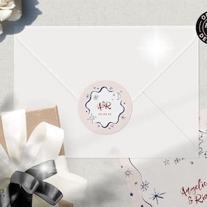May include: A pink and white round sticker with a navy blue starburst design. The sticker has the text "A&R" in red and "15.05.15" in navy blue. The sticker is on a white envelope.