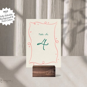 May include: A table number card with a pink and white design. The card has a handwritten number "4" in green and the text "Table No." in black. The card is on a wooden stand.