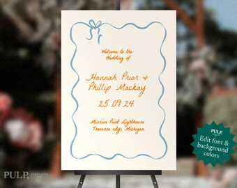 May include: A wedding welcome sign on an easel. The sign has a cream background with a blue ribbon border and text in orange script. The text reads "Welcome to the Wedding of Hannah Prior & Phillip Mackay 25.09.24 Mission Point Lighthouse Traverse city, Michigan."