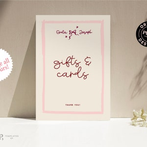 Pode incluir: Um cart&atilde;o branco com uma borda rosa e o texto "Greta & Joseph" em uma fonte manuscrita. O texto "gifts & cards" est&aacute; escrito em uma fonte manuscrita maior em cor bord&ocirc;. O texto "Thank You!" est&aacute; escrito em uma fonte menor na parte inferior do cart&atilde;o.