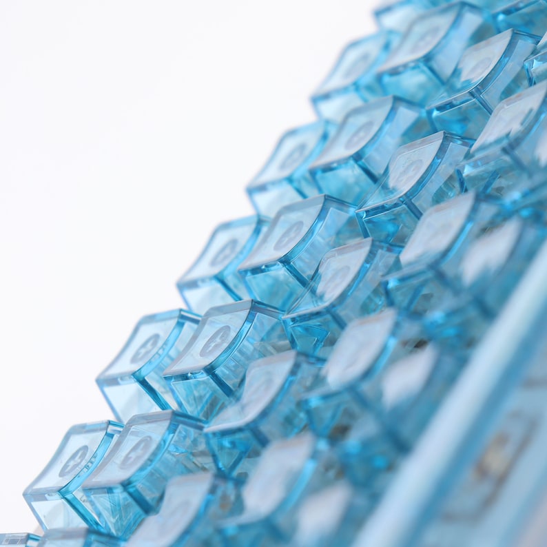 Op de afbeelding: Een close-up van een blauw toetsenbord met een geringe scherptediepte. De toetsen zijn in een verspringend patroon gerangschikt, waardoor een textuur ontstaat.