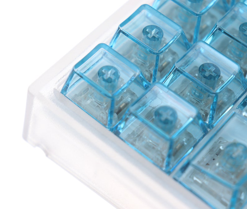 Op de afbeelding: Een close-up van een transparant plastic toetsenbord met blauwe toetsen. De toetsen hebben een plusteken erop.