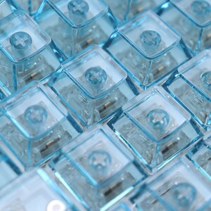 Op de afbeelding: Close-up van een groep blauwe mechanische toetsenbordtoetsen met een plusteken op elke toets.