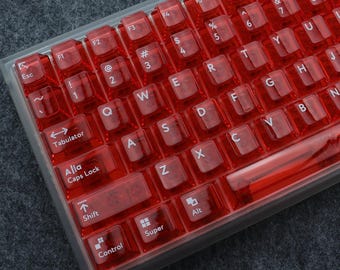May include: A red transparent keyboard with white lettering. The keys are labeled with the standard QWERTY layout, including function keys, arrow keys, and modifier keys. The keyboard has a clear plastic case.