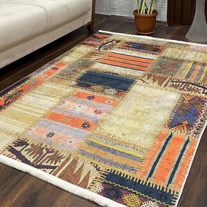 May include: A multi-colored area rug with a patchwork design featuring various geometric patterns in shades of orange, brown, blue, and beige. The rug has a white fringe border.