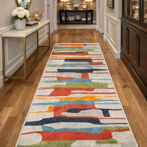 May include: A long rectangular runner rug featuring a light gray base with horizontal abstract shapes in vibrant shades of orange, navy blue, light blue, and green. The rug has a white fringe border on both ends and a low-pile textured surface.