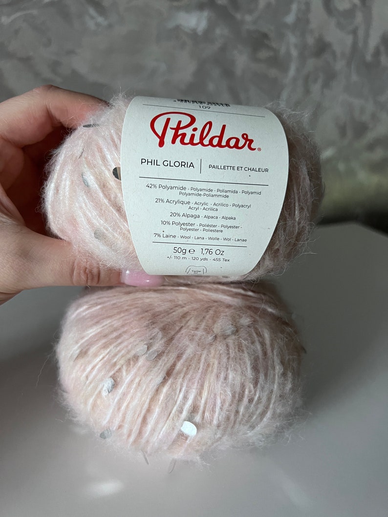 Pu&ograve; includere: Un gomitolo di filato rosa con paillettes argentate, etichettato "Phil Gloria" dal marchio "Phildar". L'etichetta indica che la composizione del filato &egrave; 42% poliammide, 21% acrilico, 20% alpaca, 10% poliestere e 7% lana. Il filato pesa 50 grammi e fa 1,76 once.