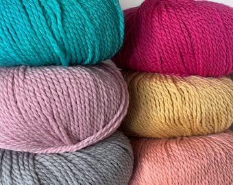 May include: Five balls of yarn stacked on top of each other. The yarn is in different colors: teal, pink, yellow, peach, and gray.