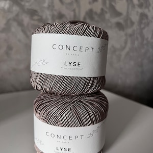 Pode incluir: Duas meadas de fio Katia Concept Lyse, feitas de linho e algodão. O fio é uma mistura de fios castanhos e brancos, criando uma aparência texturizada. Cada meada tem uma etiqueta branca com o nome da marca e o tipo de fio.
