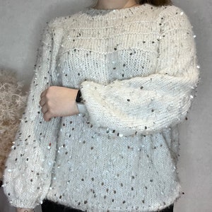 Pu&ograve; includere: Maglia di lana bianca con paillettes argentate. La maglia ha un collo rotondo e maniche lunghe.