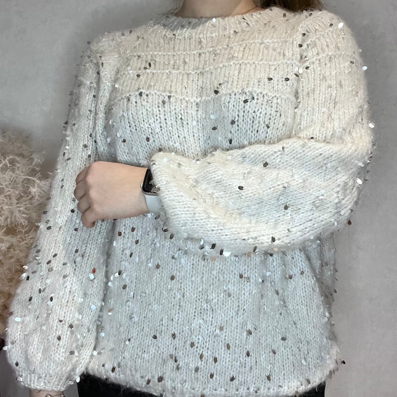 Pu&ograve; includere: Maglia di lana bianca con paillettes argentate. La maglia ha un collo rotondo e maniche lunghe.