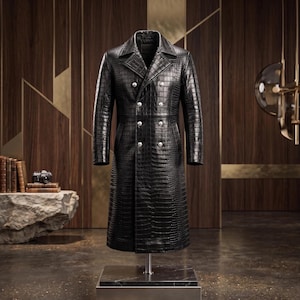 May include: A long, double-breasted black coat featuring a textured crocodile skin pattern. The garment includes a wide notched lapel, long sleeves, and two vertical rows of six polished silver-toned buttons down the front centre.