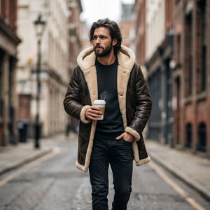 May include: A dark brown leather hooded coat with a thick cream-colored shearling lining, worn over a black long-sleeve shirt and dark denim jeans. The coat features a front opening, long sleeves, and a hood, while a white paper coffee cup is held.