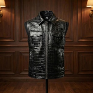 Può includere: Un gilet in pelle nera con una texture a pelle di coccodrillo. Il gilet ha un collo, due tasche sul petto e una cerniera a tutta lunghezza. Viene esposto su un manichino.