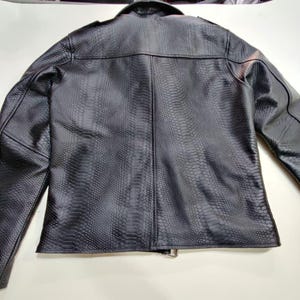 Może przedstawiać: Czarna kurtka ze sztucznej sk&oacute;ry z fakturą sk&oacute;ry węża. Kurtka ma klasyczny kr&oacute;j z kołnierzem, naramiennikami i zapięciem na zamek błyskawiczny. Widok z tyłu pokazuje dopasowany kr&oacute;j i szczeg&oacute;łowe szwy.