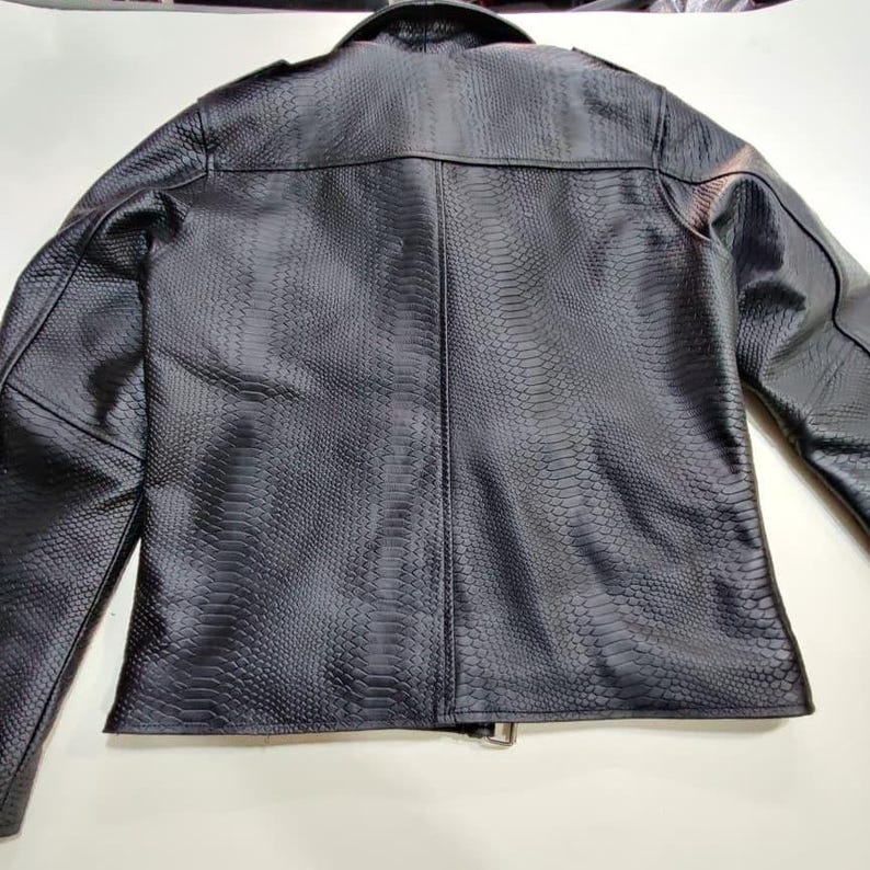 Może przedstawiać: Czarna kurtka ze sztucznej sk&oacute;ry z fakturą sk&oacute;ry węża. Kurtka ma klasyczny kr&oacute;j z kołnierzem, naramiennikami i zapięciem na zamek błyskawiczny. Widok z tyłu pokazuje dopasowany kr&oacute;j i szczeg&oacute;łowe szwy.