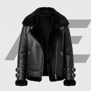May include: A black leather jacket with a thick black faux fur lining and collar. The jacket features gold-toned metal zips, a diagonal front closure, and two adjustable buckle straps on each sleeve cuff. A black turtleneck is worn underneath.