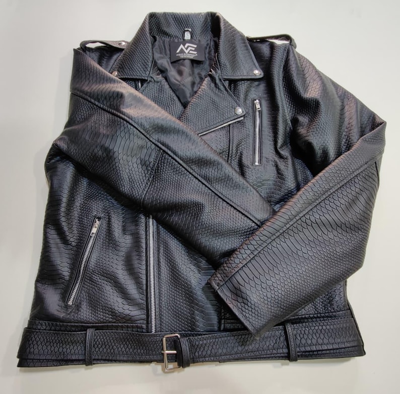 Może przedstawiać: Czarna kurtka ze sztucznej sk&oacute;ry o fakturze sk&oacute;ry węża. Kurtka posiada kołnierz z klapami, liczne kieszenie zapinane na zamek oraz pasek ze srebrną klamrą. Kurtka ma klasyczny styl motocyklowy.