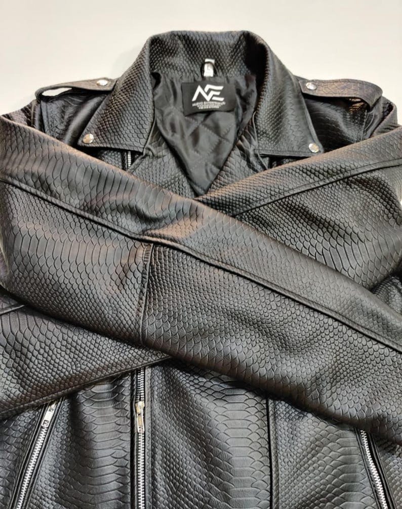 Może przedstawiać: Czarna kurtka ze sztucznej sk&oacute;ry o fakturze sk&oacute;ry węża. Kurtka posiada kołnierz z klapami, srebrne zamki błyskawiczne i pikowaną podszewkę. Logo marki jest widoczne na metce wewnątrz kurtki.