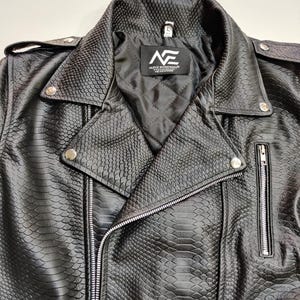 Może przedstawiać: Czarna kurtka motocyklowa ze sztucznej sk&oacute;ry o fakturze sk&oacute;ry węża. Kurtka posiada kołnierz z klapami, srebrne zamki błyskawiczne i zatrzaski. Wewnętrzna podszewka jest czarna i pikowana. Widoczne jest logo marki "NE".